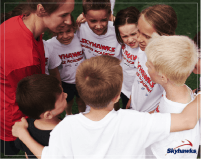 A group of kids putting their hands together at a Skyhawks camp.